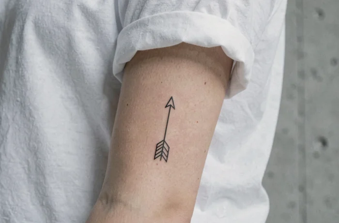 Tatouage flèche minimaliste en encre noire sur l'avant-bras intérieur d'une femme
