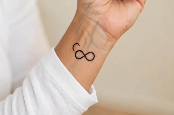 Tatouage symbole de l'infini en encre noire fine sur le poignet intérieur d'une femme
